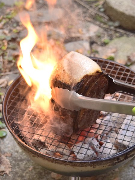 豚肉をトングで支えながら炭火で焼く